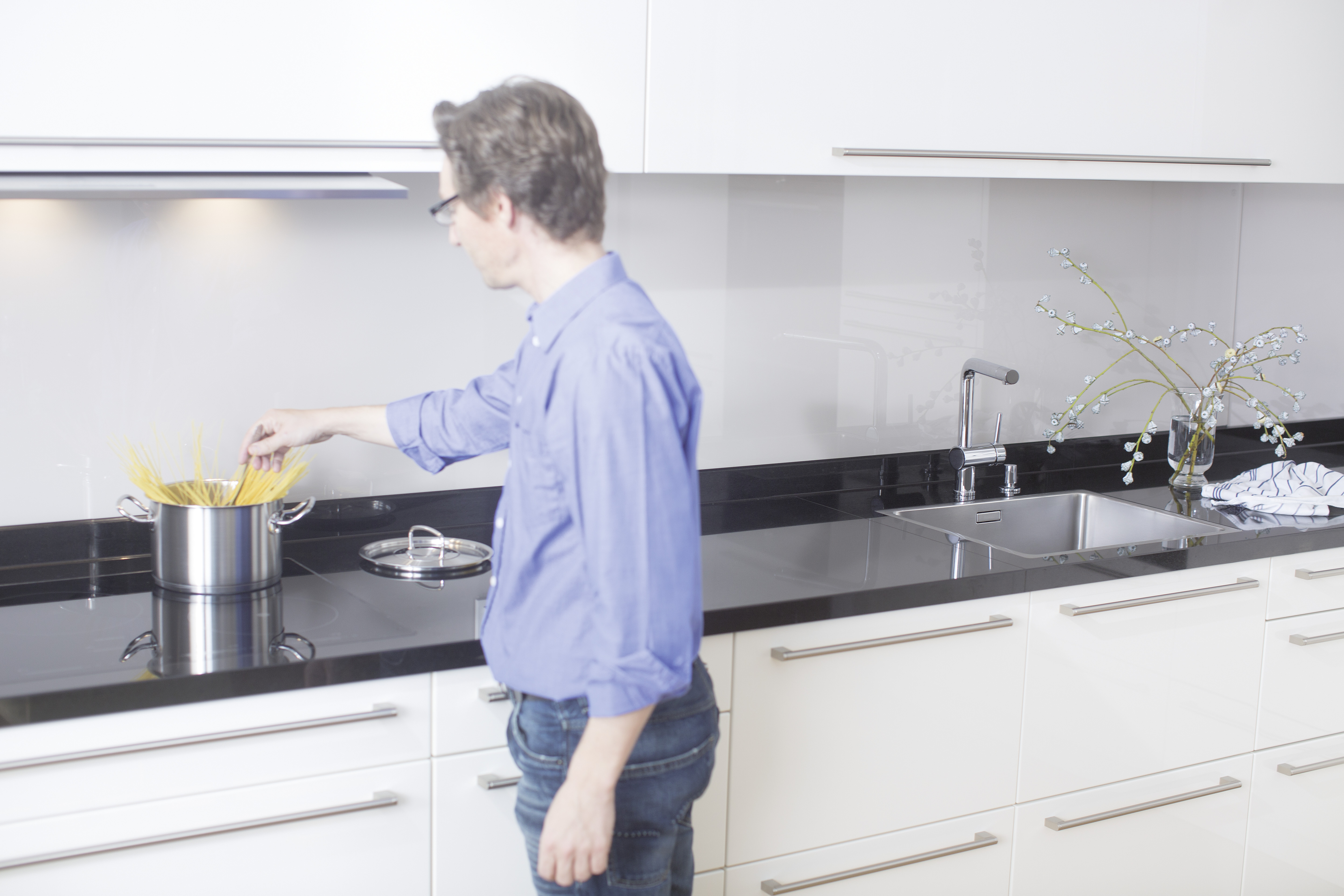 A man puts pasta in a high pot, it's on the stove.