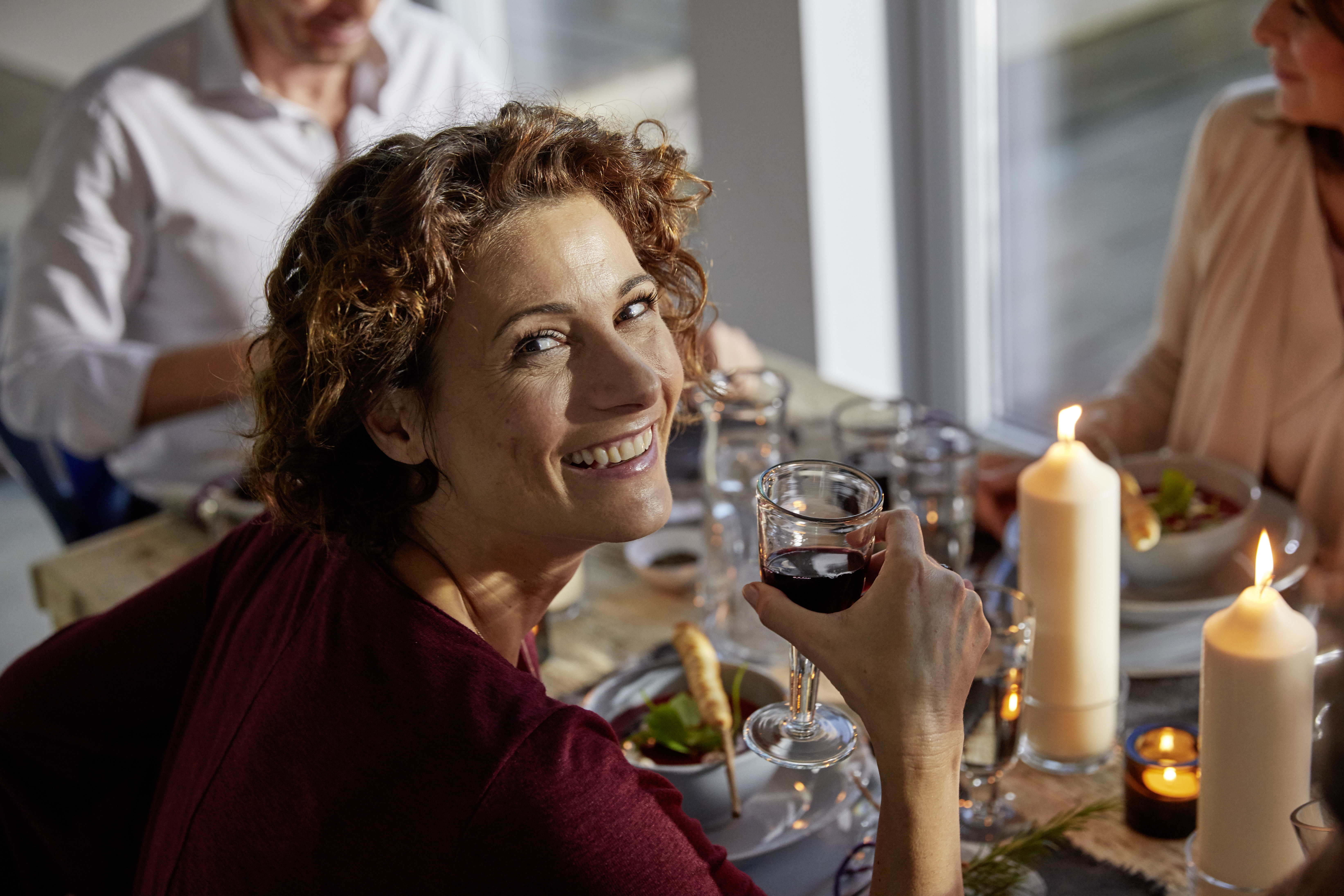A woman looks happily into the camera and holds a wine glass in her hand