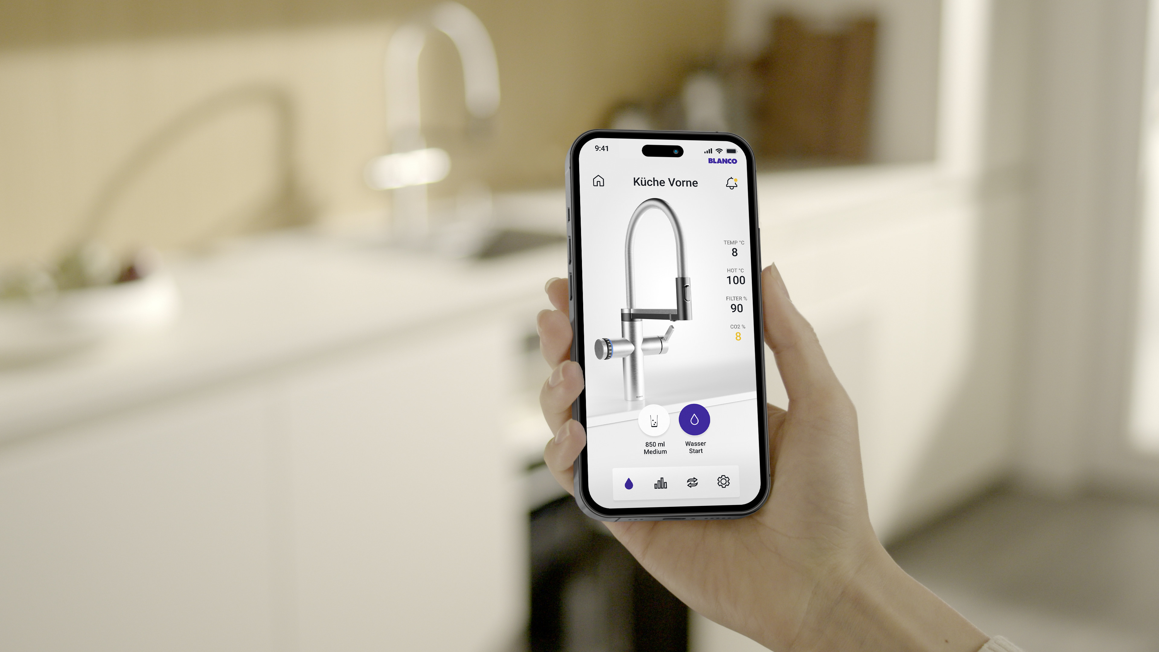 Une personne tient un smartphone à la main, tandis qu'on aperçoit un robinet de cuisine en arrière-p