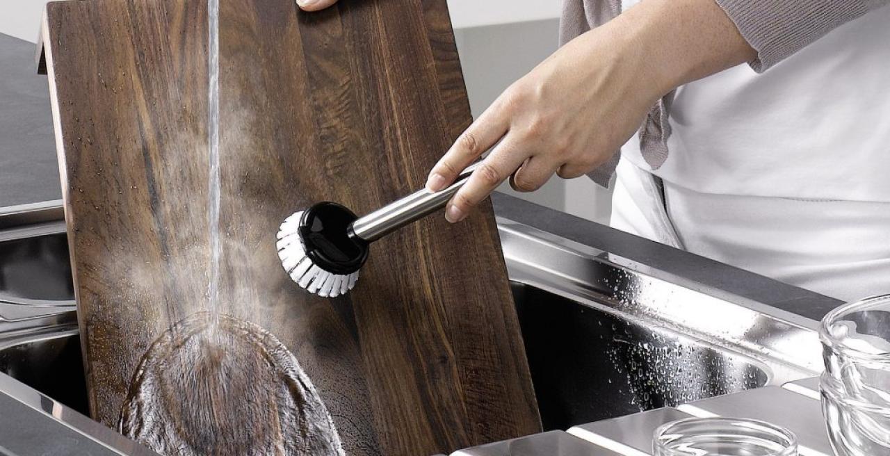 Ein dunkles Schneidebrett wird in einer Edelstahlspüle gereinigt