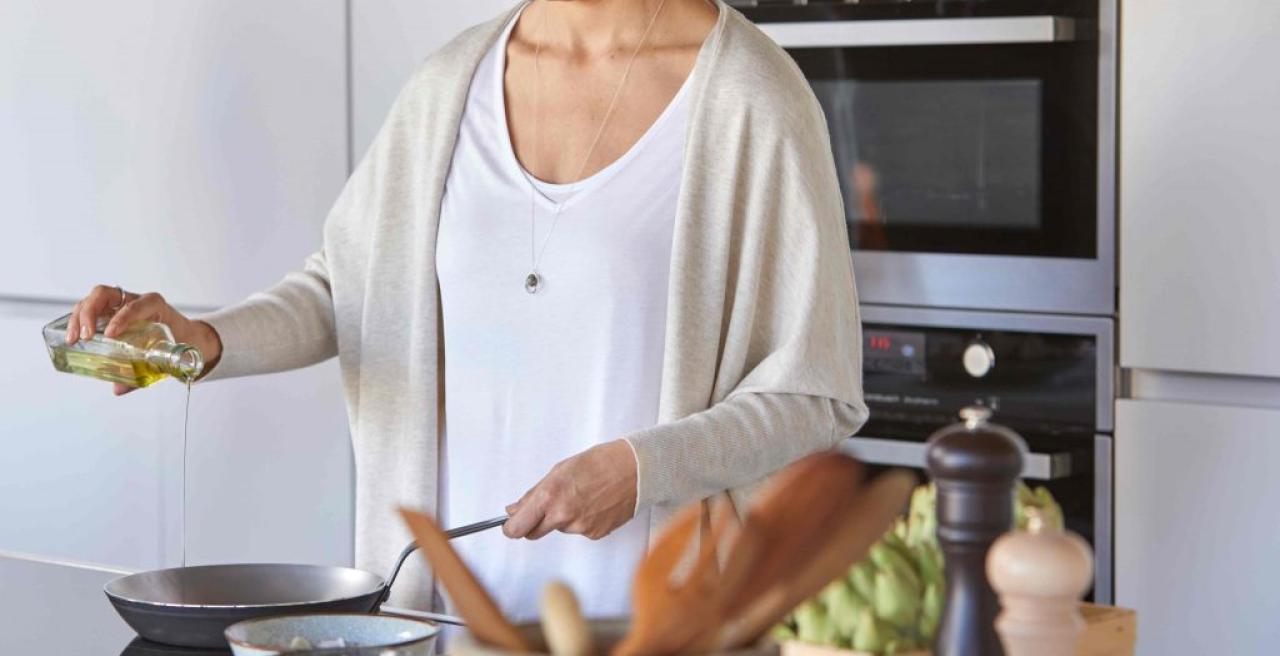 Eine Frau kocht, im Vordergrund stehen Kochutensilien aus Holz
