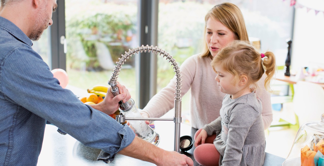 Father and mother are standing around the sink, a little girl is sitting beside the sink
