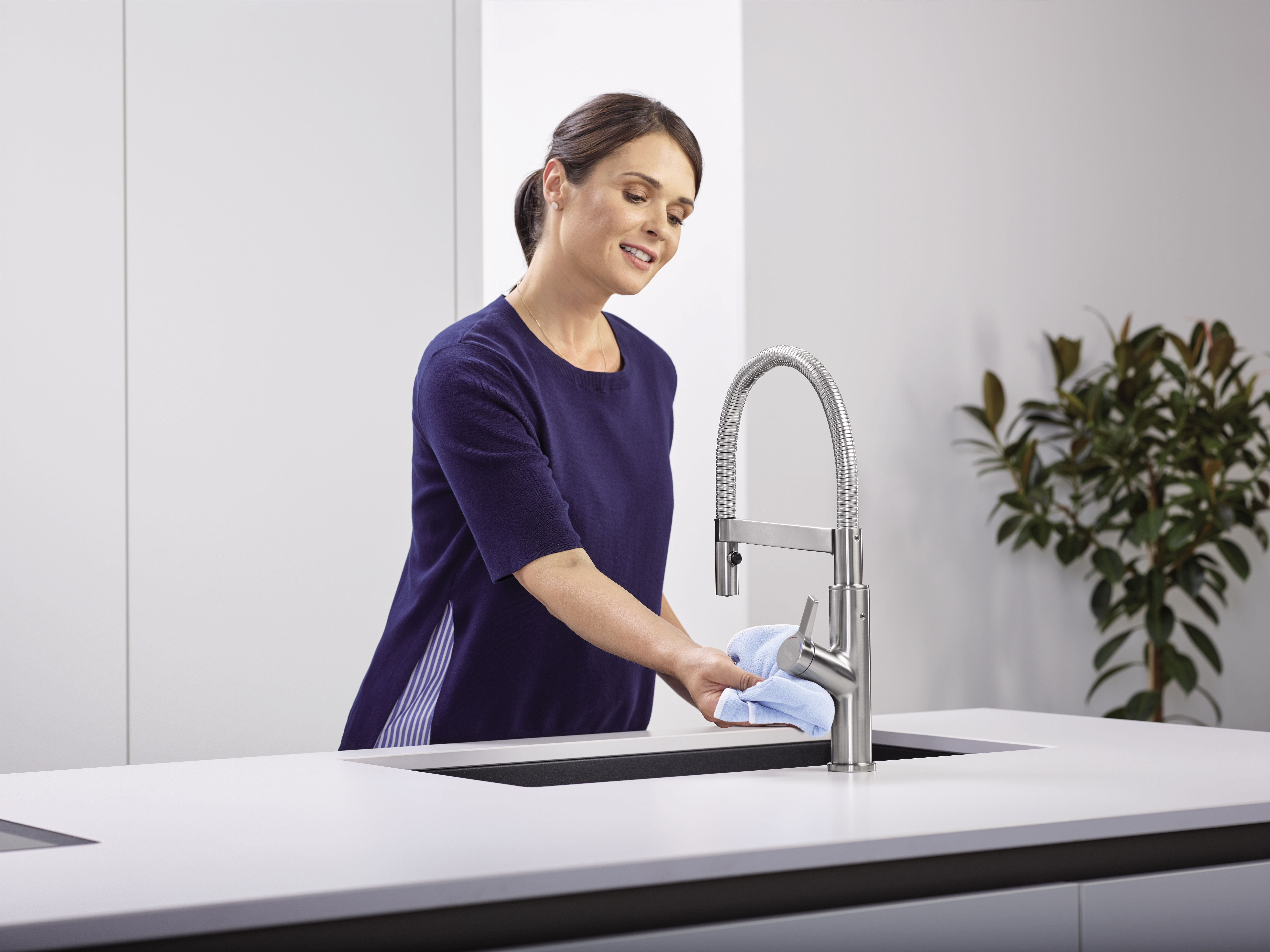 Een huisvrouw maakt de mengkraan schoon met een microvezeldoek.